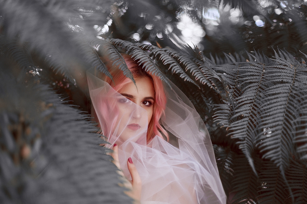 Mujer de pelo rosa dentro de un bosque de palmeras grises.
