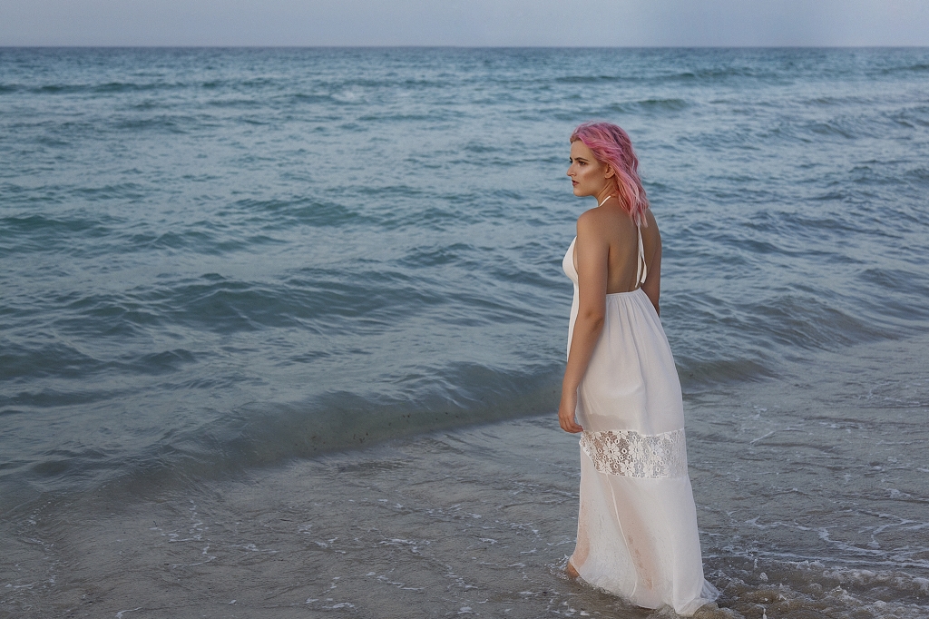 Mujer vestida de blanco en la orilla de la playa entrando al mar.