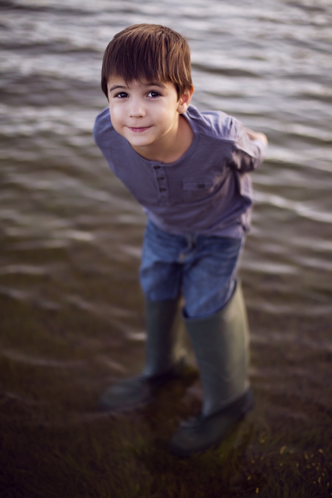 Niño dentro del agua con botas de pescador.