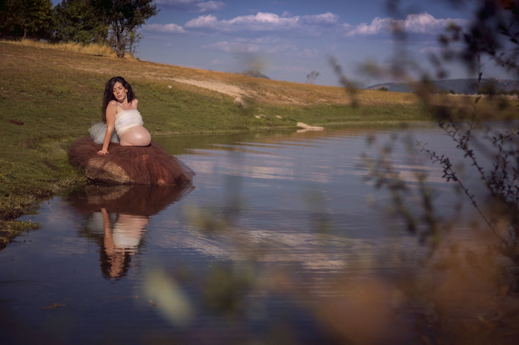 Mujer embarazada sentada en una roca a la orilla del agua.
