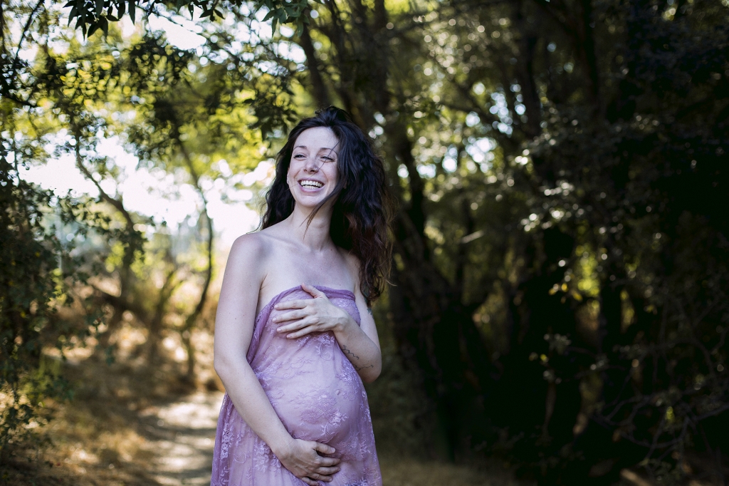Mujer embarazada sonriendo dentro de un bosque.