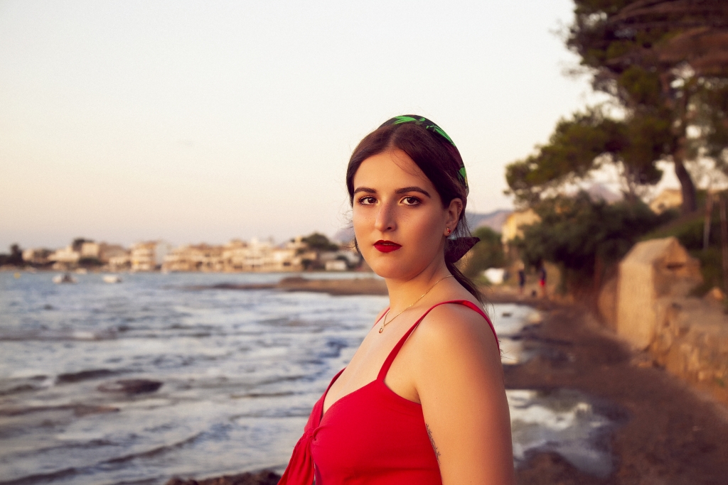 Mujer al borde del mar con vestido rojo y la mirada perdida.