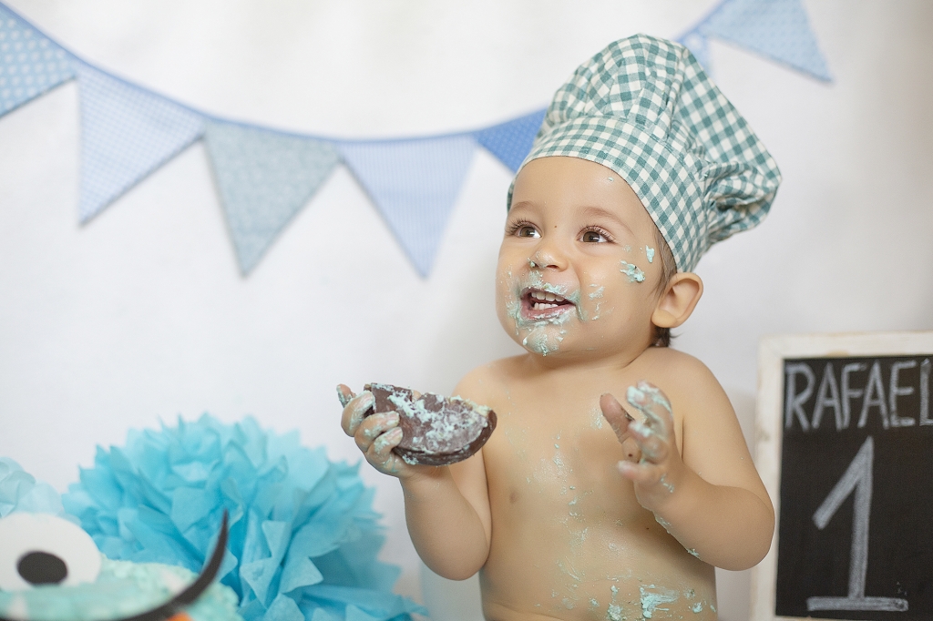 Niño con gorro de cocinero en su primer cumpleaños con banderines, globo y tarta.