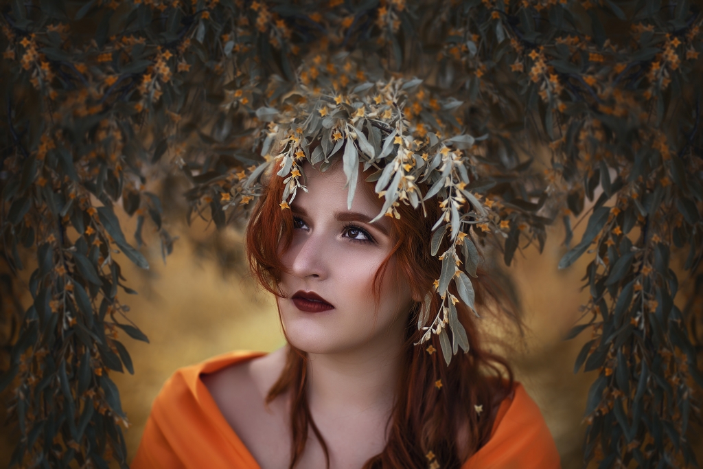 retrato de mujer en el bosque rodeada de flores naranjas.