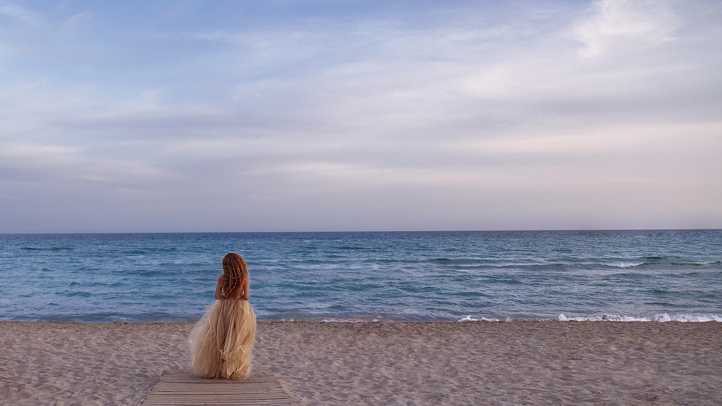 Mujer en la arena de la playa mirando al mar.