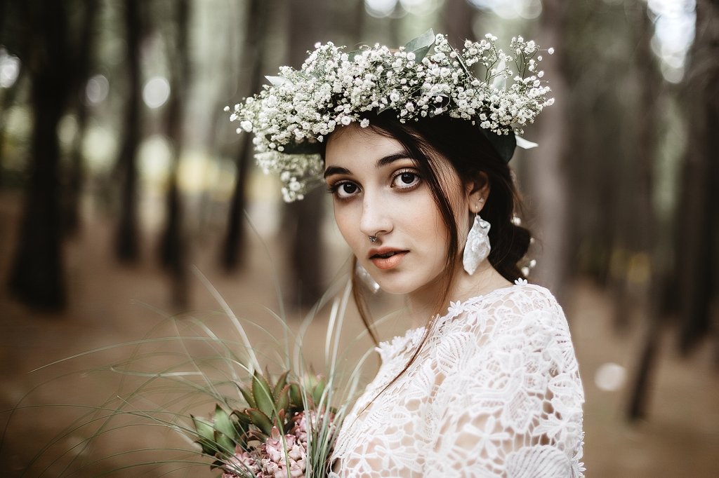 Retrato de novia en medio de un bosque con corona de flores blancas.