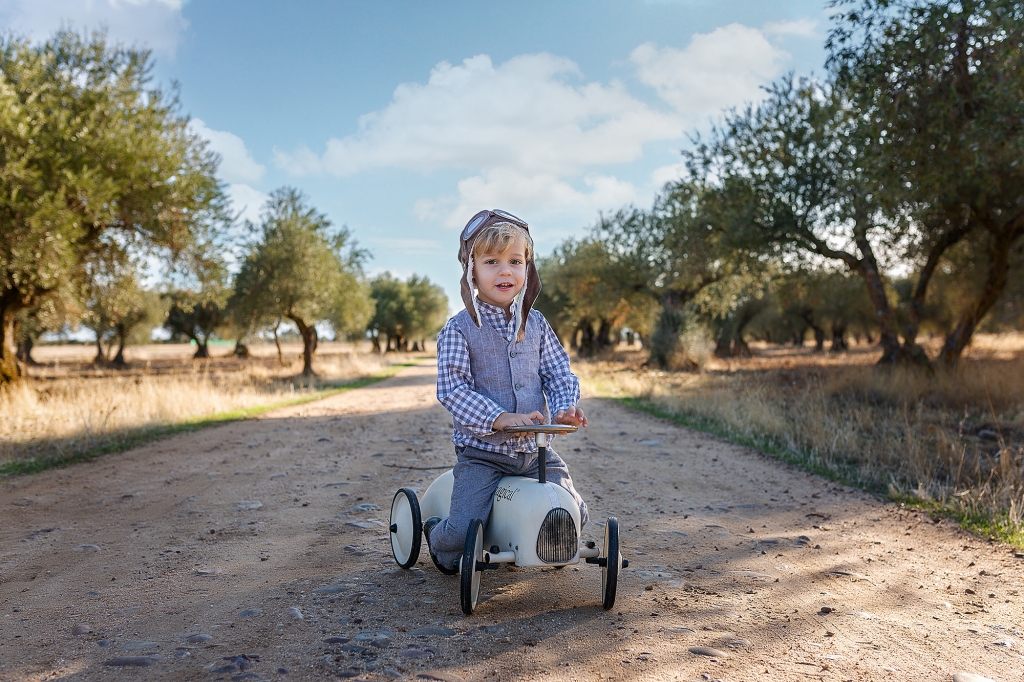 Niño subido a un cochecito en medio de un campo de olivos.