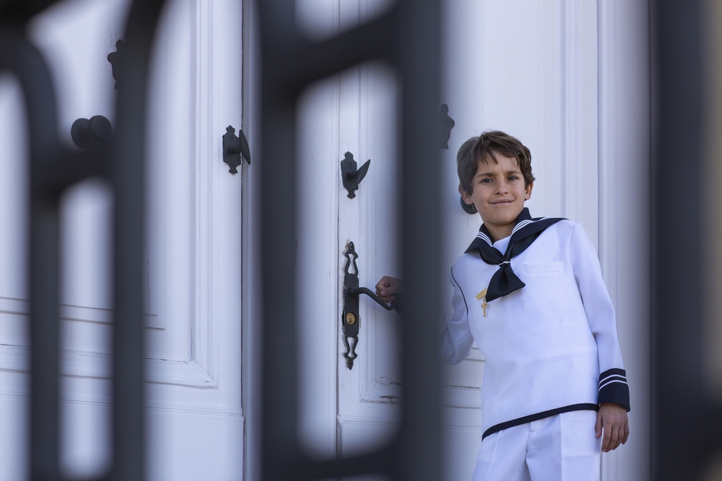 Niño de Comunión con traje de marinero en una puerta blanca.