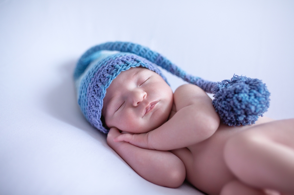 Recién nacida dormida con gorrito de lana con borla azul.