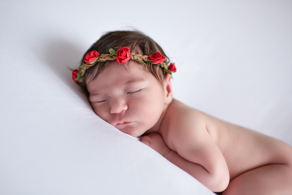 Recién nacida dormida con corona de flores rojas.