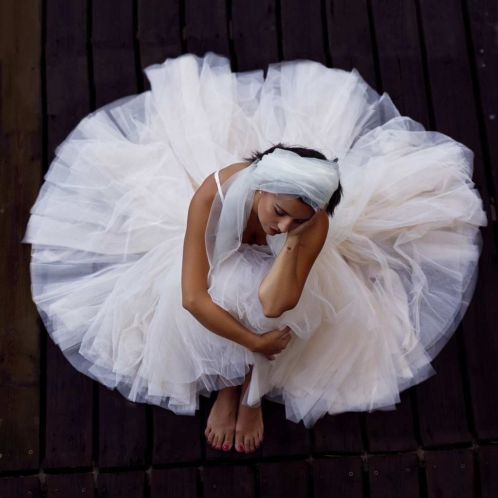 Bailarina con tutú blanco sentada sobre un suelo de madera oscura.