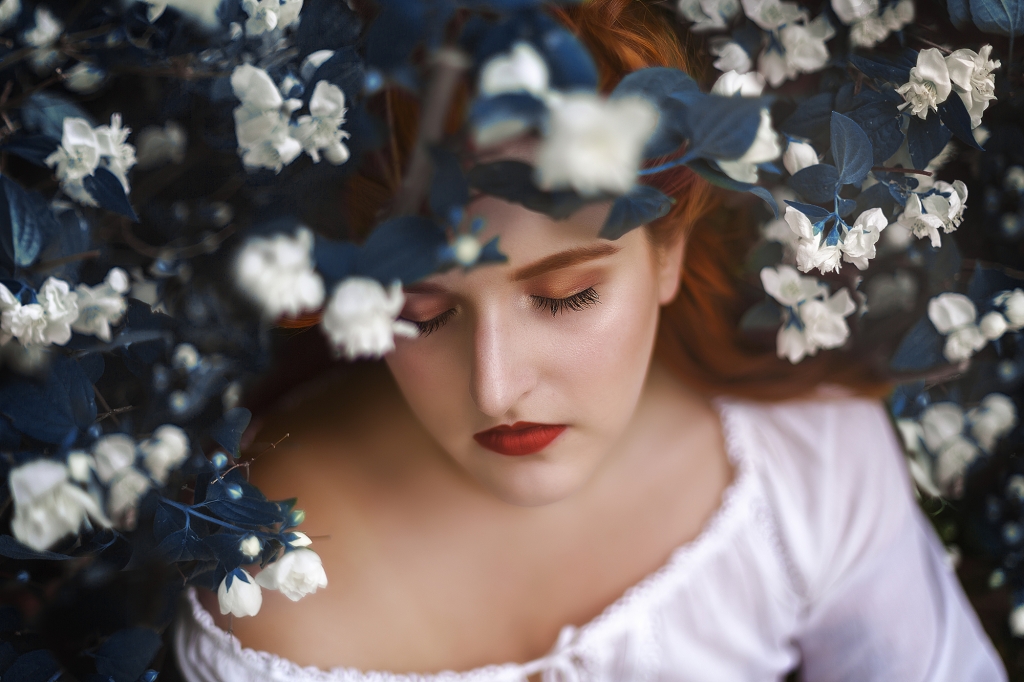 Retrato chica pelirroja rodeada de flores blancas.