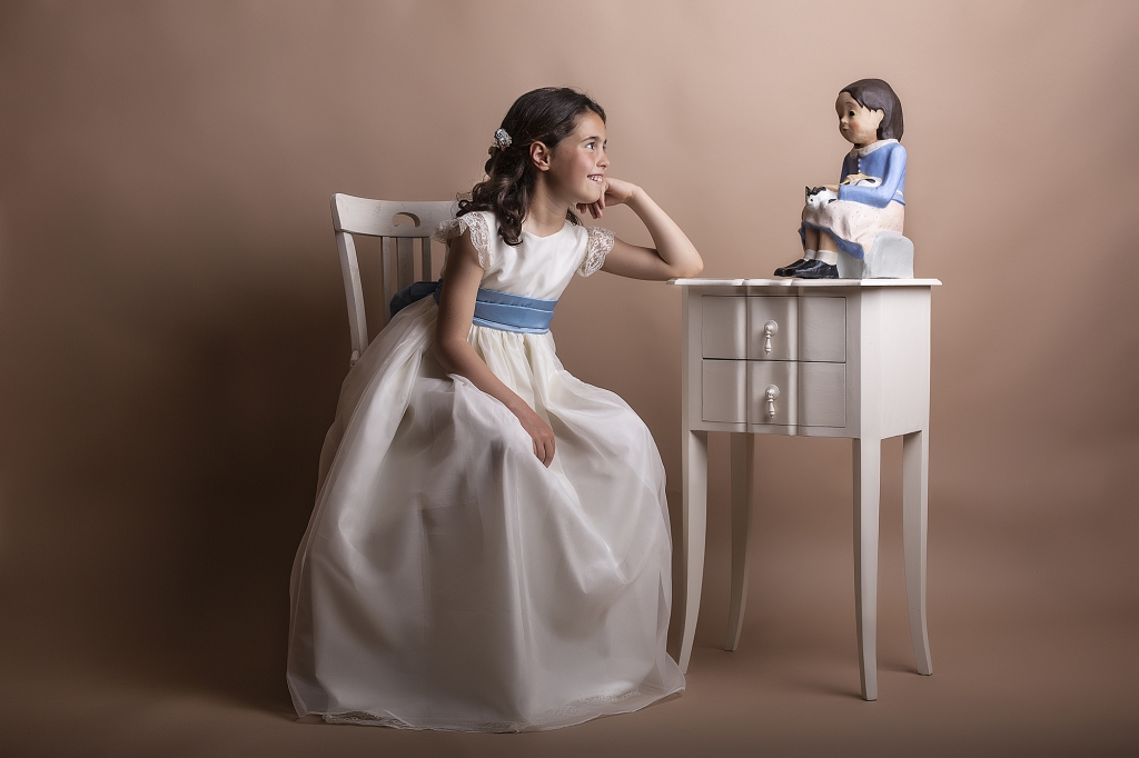Niña de Comunión sentada mirando una muñeca vestida de azul.
