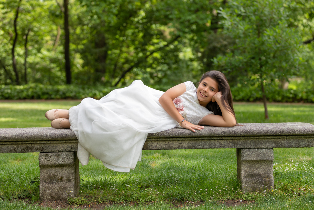 Niña de Comunión tumbada en un banco de piedra en un parque.