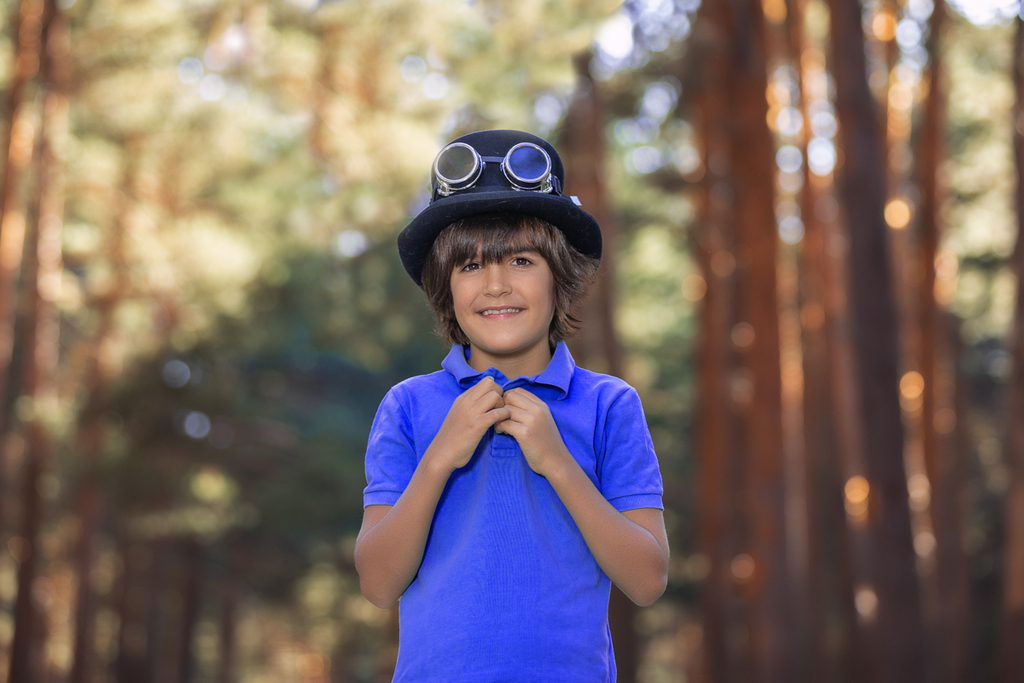 Niño en el bosque con sombrero de copa y gafas de aviador.