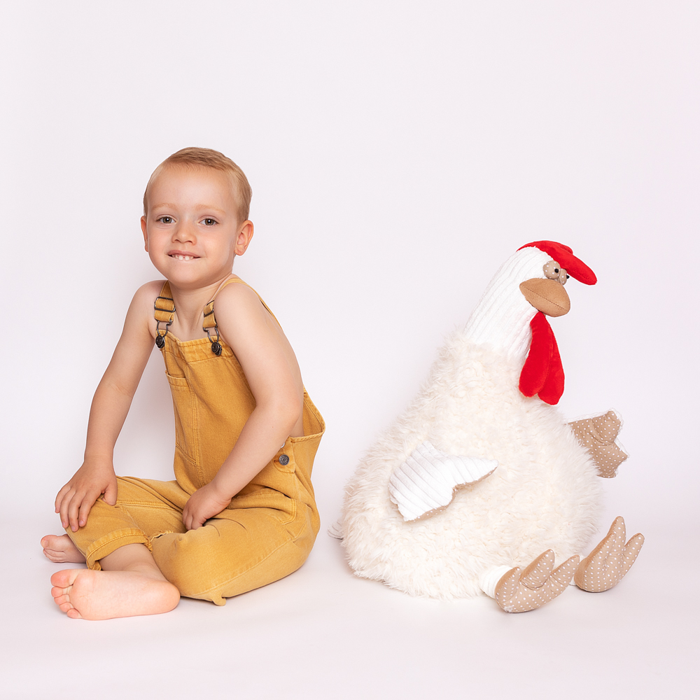 Niño con pantalón amarillo junto a un gallo de peluche.